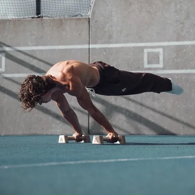 Athlete performing planche lean on Caliathletics parallettes outdoors
